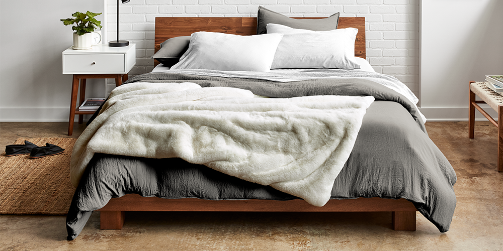 Bed with a cream faux fur blanket next to a wood nightstand