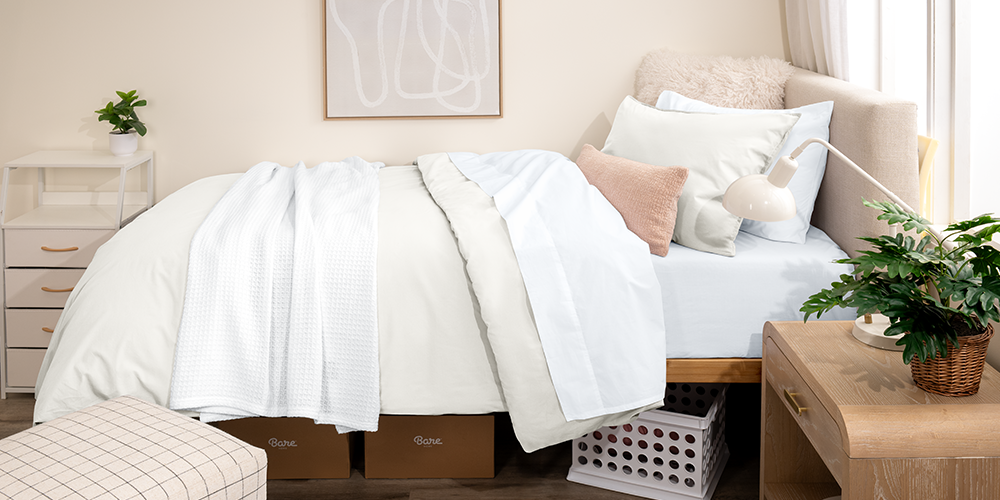 Bed styled with white Organic Cotton Percale Dorm Bundle in a dorm room setting with plant