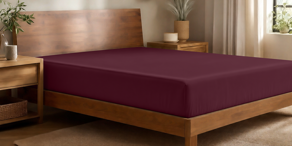 Bed with a burgundy bamboo fitted sheet on a wood bed frame