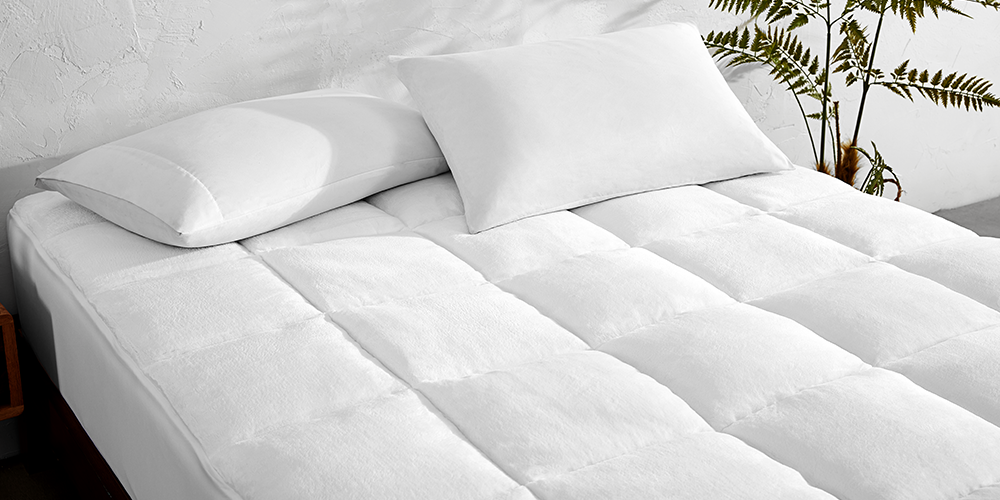 Bed styled with white quilted Reversible Mattress Pad, plant nearby