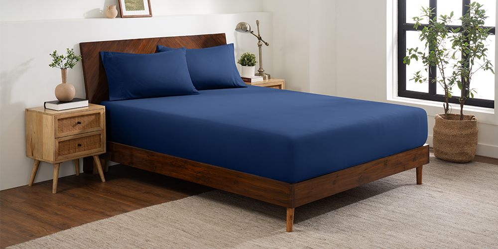 Bed styled with navy blue Ultra Soft Fitted Sheet with Pillowcase Set and wood nightstand