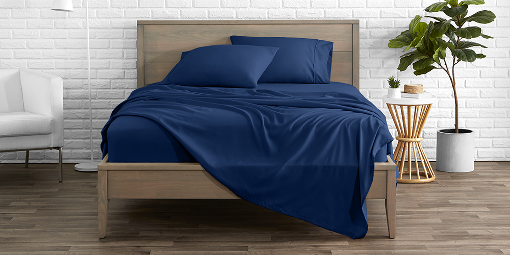 Bed styled with navy blue Ultra Soft Flat Sheet, plant nearby