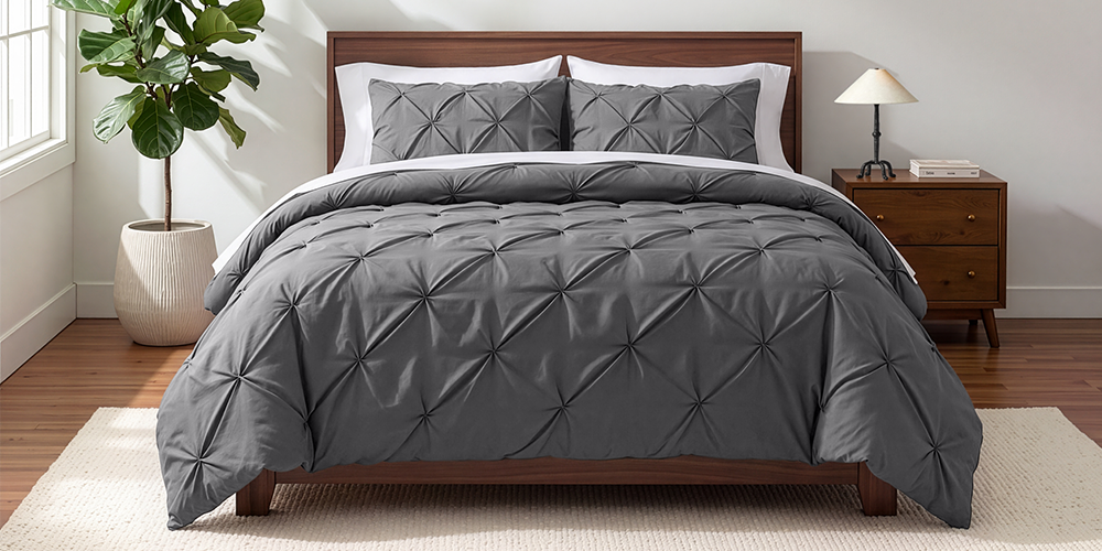 Bed styled with dark gray Ultra Soft Pintuck Comforter Set, wood nightstand, plant nearby