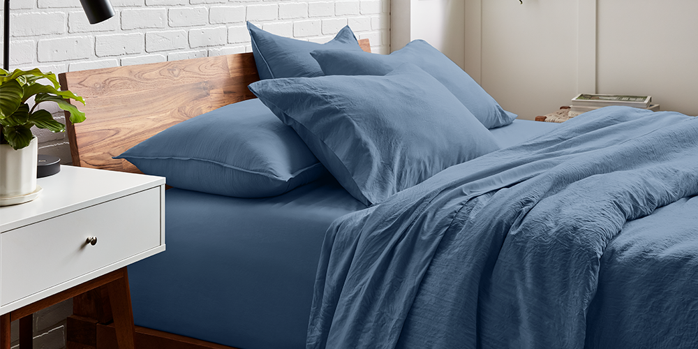 Bed styled with denim blue Ultra Soft Washed Bedding Bundle, wood nightstand, plant nearby