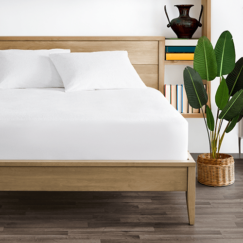 Bed styled with white Cotton Terry Mattress Protector, closeup with plant nearby