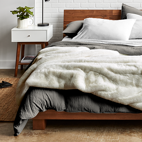 Bed with a cream faux fur blanket next to a wood nightstand