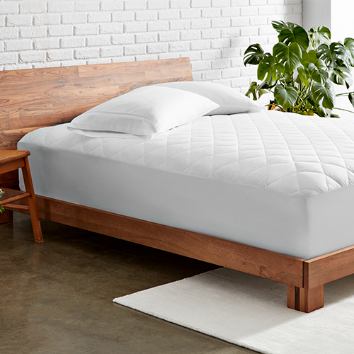 Bed styled with white Quilted Mattress Pad and wood bed frame in a bedroom
