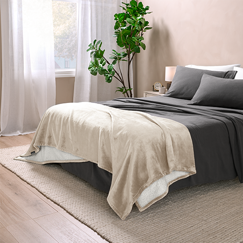 Bed with tan Sherpa Blanket at the foot and gray sheets