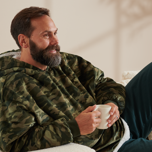 Man wearing a camo Bare Homey Wearable Blanket (Sherpa Adult), sitting
