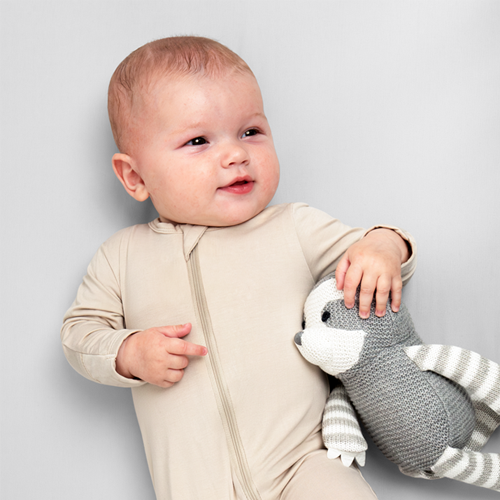 Baby sitting on a cream crib sheet with a stuffed animal