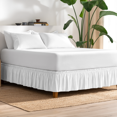 Bed with a white wrap-around bed skirt next to a plant