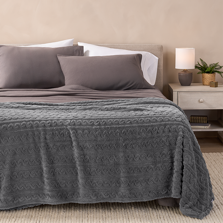 Close-up of gray cable knit faux shearling blanket draped on a bed