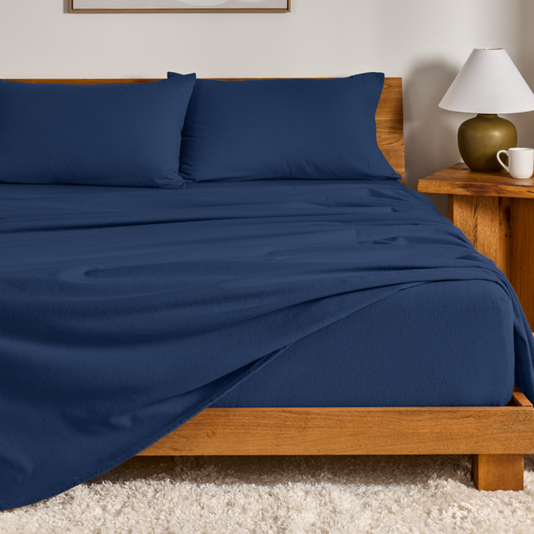 Blue bed sheets and pillows on a wooden bed with a nightstand in the background.