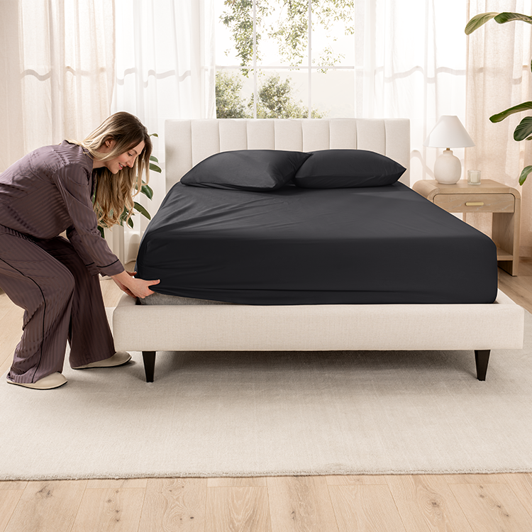 Woman fitting black Organic Cotton Sateen Fitted Sheet onto a mattress corner