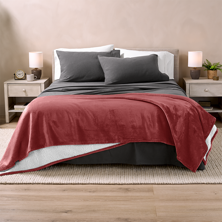 Bed with dark red Sherpa Blanket at the foot and gray pillows