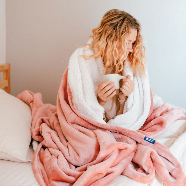 Woman drinking coffee wrapped in a pink sherpa blanket