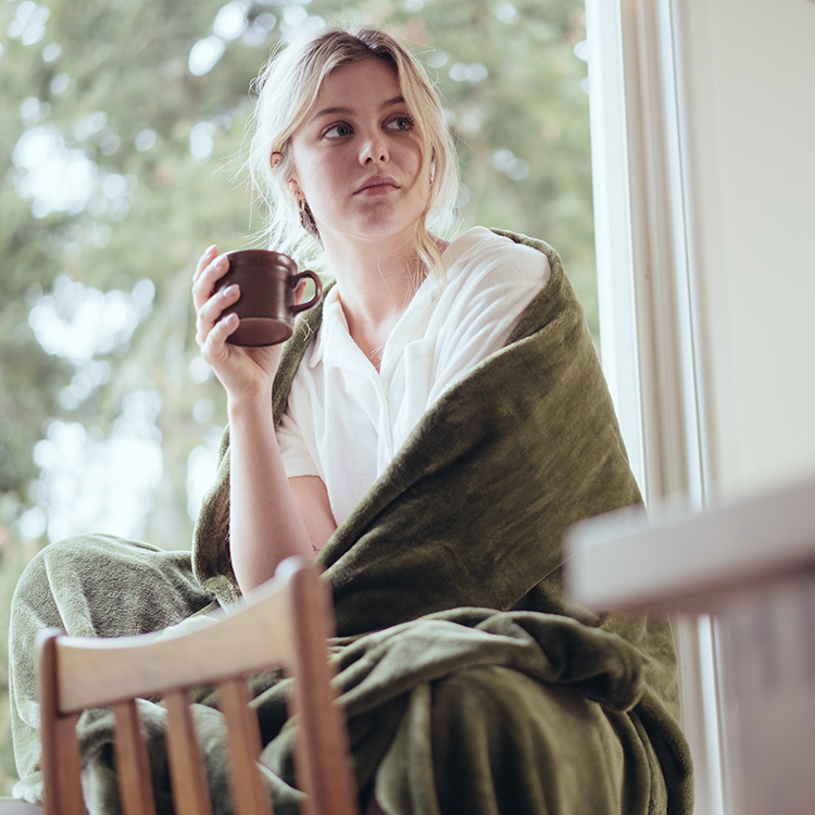 Man wrapped in an olive green blanket sitting on a couch, digital gift card photo