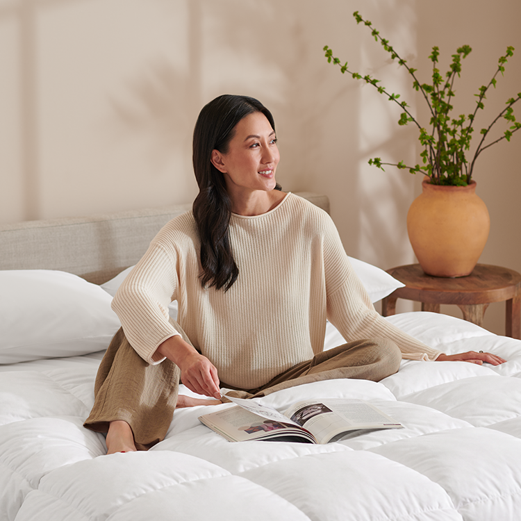 Woman sitting on a bed wrapped in a cream blanket with a dog nearby