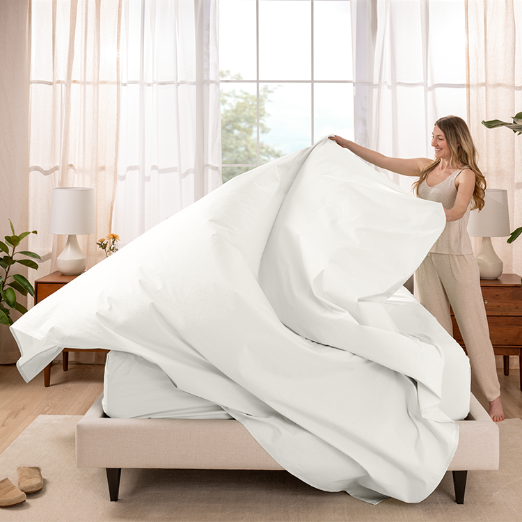 Woman making a bed with white Organic Cotton Percale Sheet Set near a sunlit window