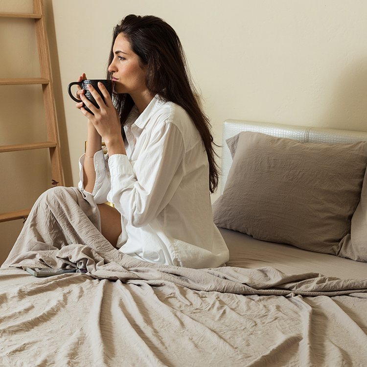 Woman sitting in bed with white Ultra Soft Washed Sheet Set, holding a mug