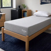 A light gray Bare Home mattress on a wooden bed frame in a modern dorm room