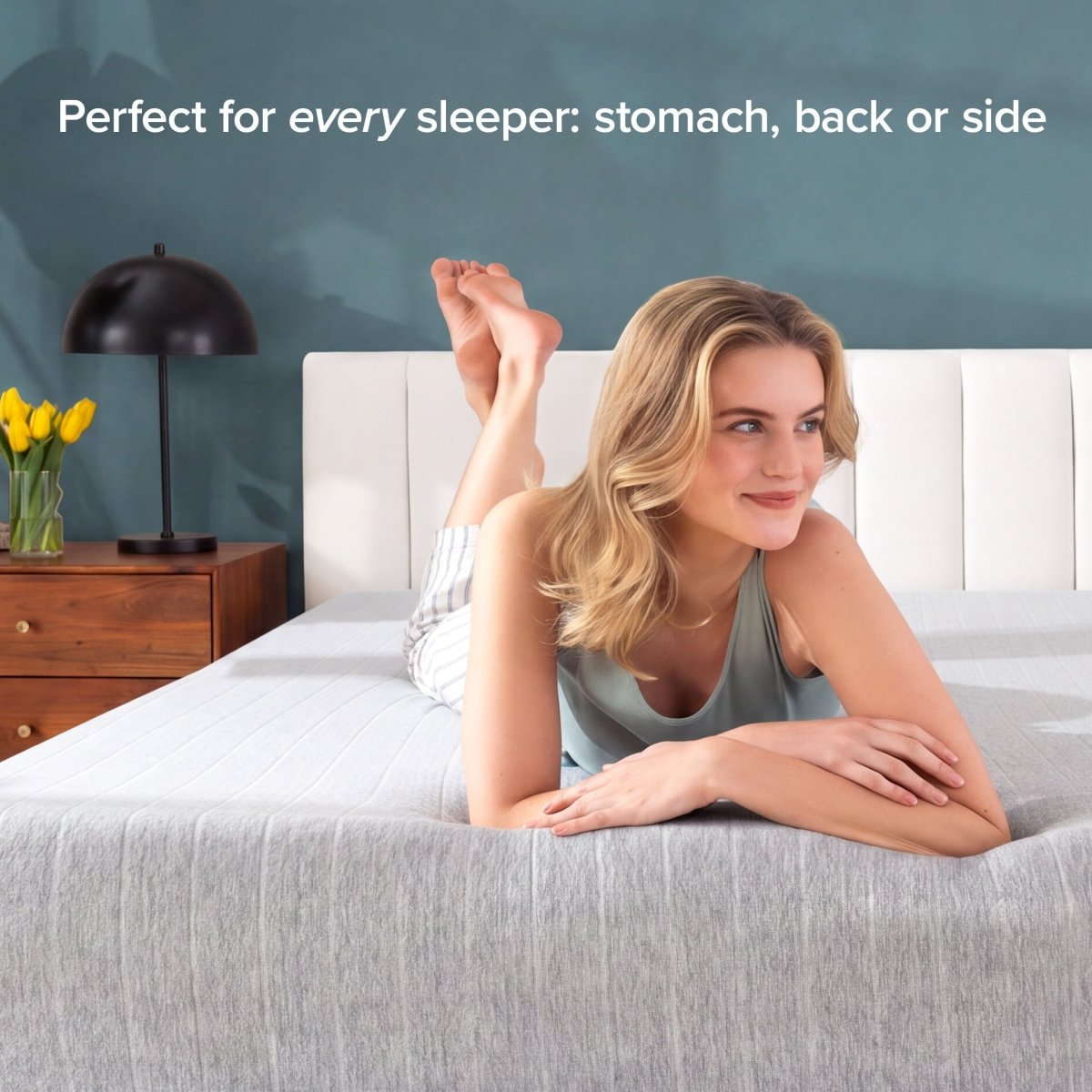 A woman lies on her stomach on a bed with a textured gray mattress, in a bedroom setting