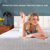 A woman lies on her stomach on a bed with a textured gray mattress, in a bedroom setting