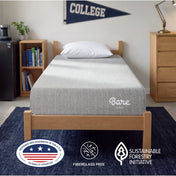 A light gray textured mattress on a wooden bed frame in a dorm room setting, with a COLLEGE pennant and a mini fridge in the background