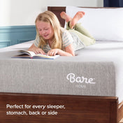 A young girl lies on her stomach on a mattress, reading a book.