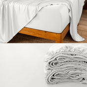A fitted sheet on a mattress with wooden bed frame and folded on a dark surface