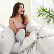 Woman sitting on a bed under duvet cover with a plant in the background