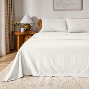 A bed dressed in flannel sheet set in a bedroom with a wooden headboard, bedside table and lamp