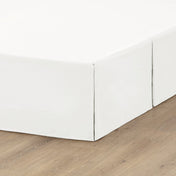 The corner of a box spring with a pleated bed skirt on it