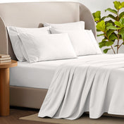 Bed sheets and pillows on a bed with a plant and side table in the background.