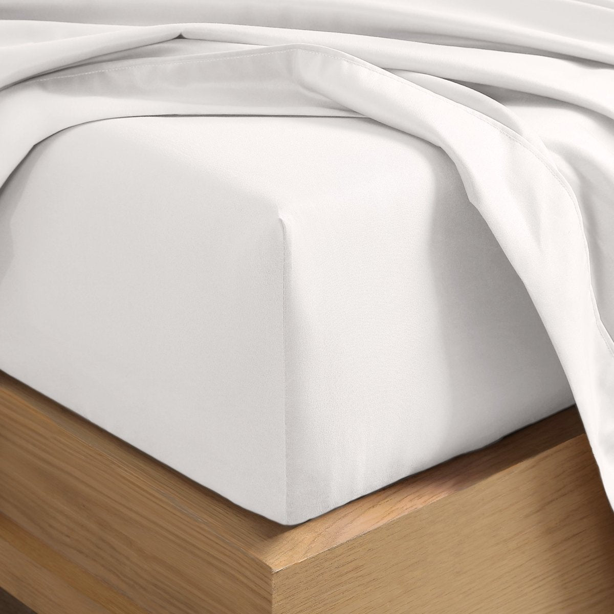 A close-up of a fitted sheet covering the corner of a bed frame, with matching top sheet draped over it.