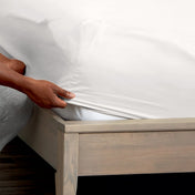 A man is putting a fitted sheet on a bed