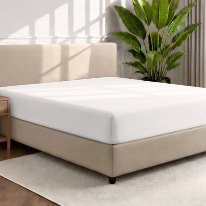 Bed with a fitted sheet in a room with a large plant and rug