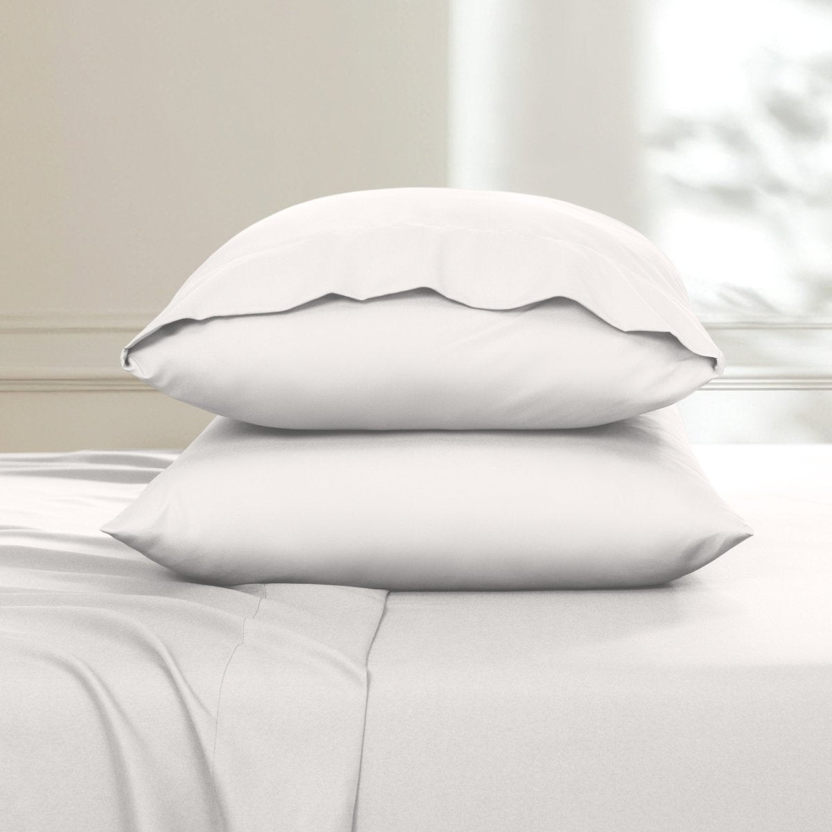 Two pillows stacked on a bed with a neutral background