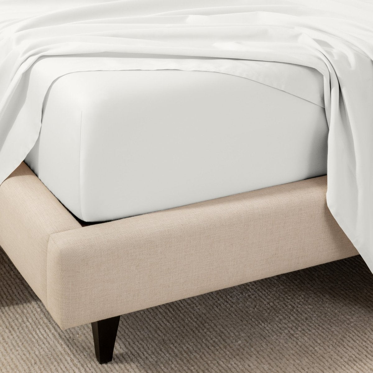 A close-up of the corner of a bed with a fitted sheet and matching flat sheet.
