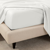 A close-up of the corner of a bed with a fitted sheet and matching flat sheet.