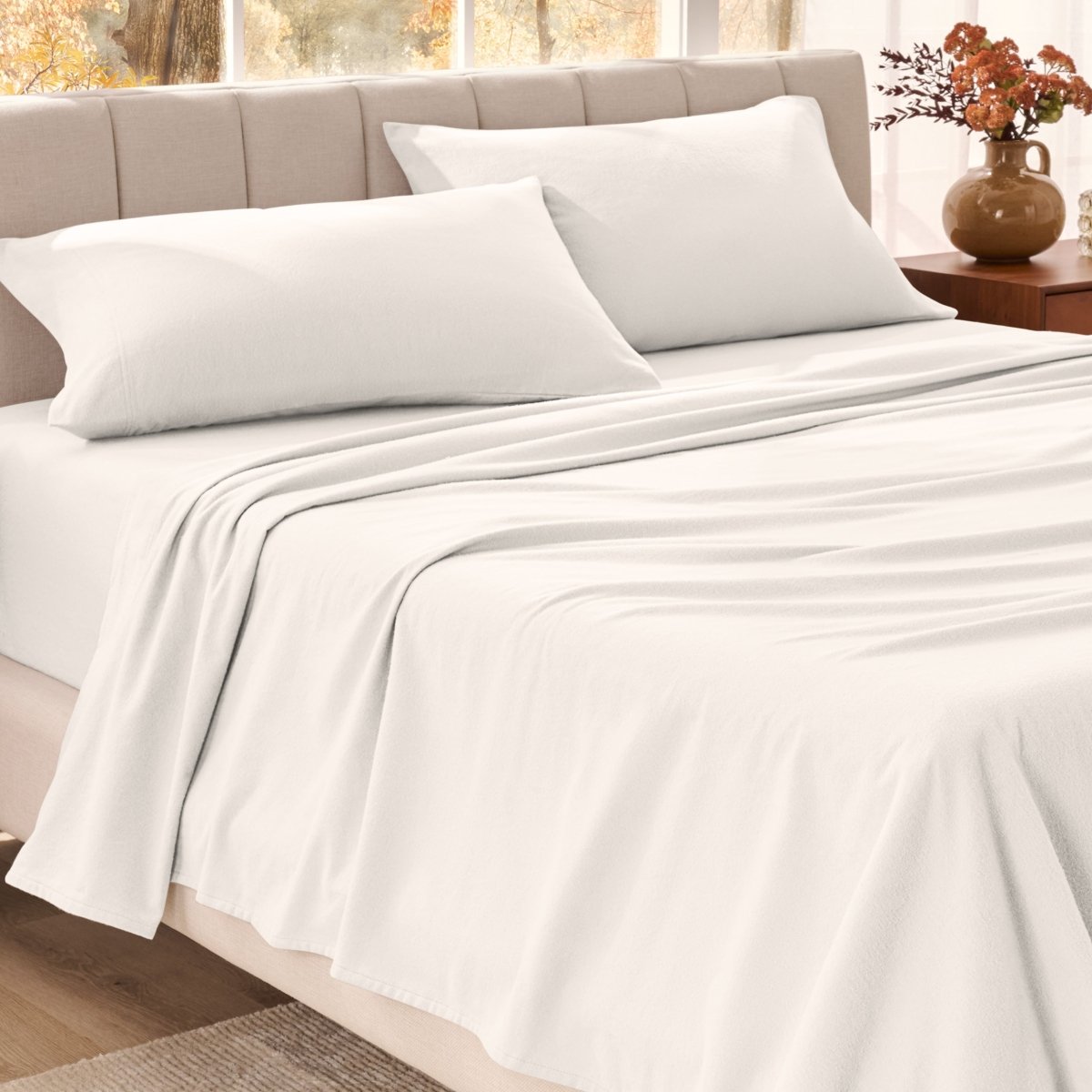 Bed sheets on a neatly made bed in a bright bedroom with large windows.