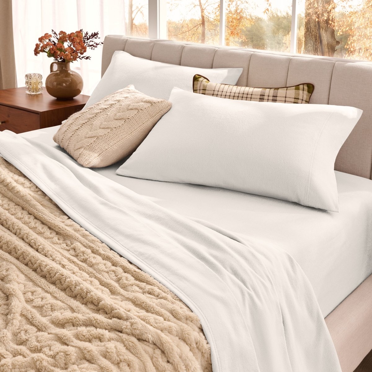 Neatly made bed with organic flannel sheets  and a beige blanket in a bright bedroom.