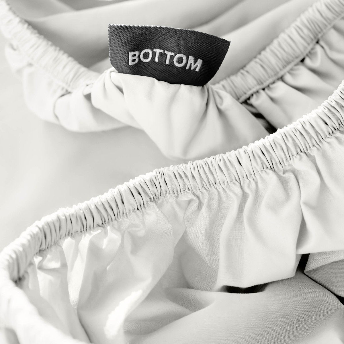 Close-up of a fitted sheet with a black fabric brand label reading BOTTOM.