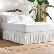 Bed with bed skirt, white bedding, and a plant in a room.