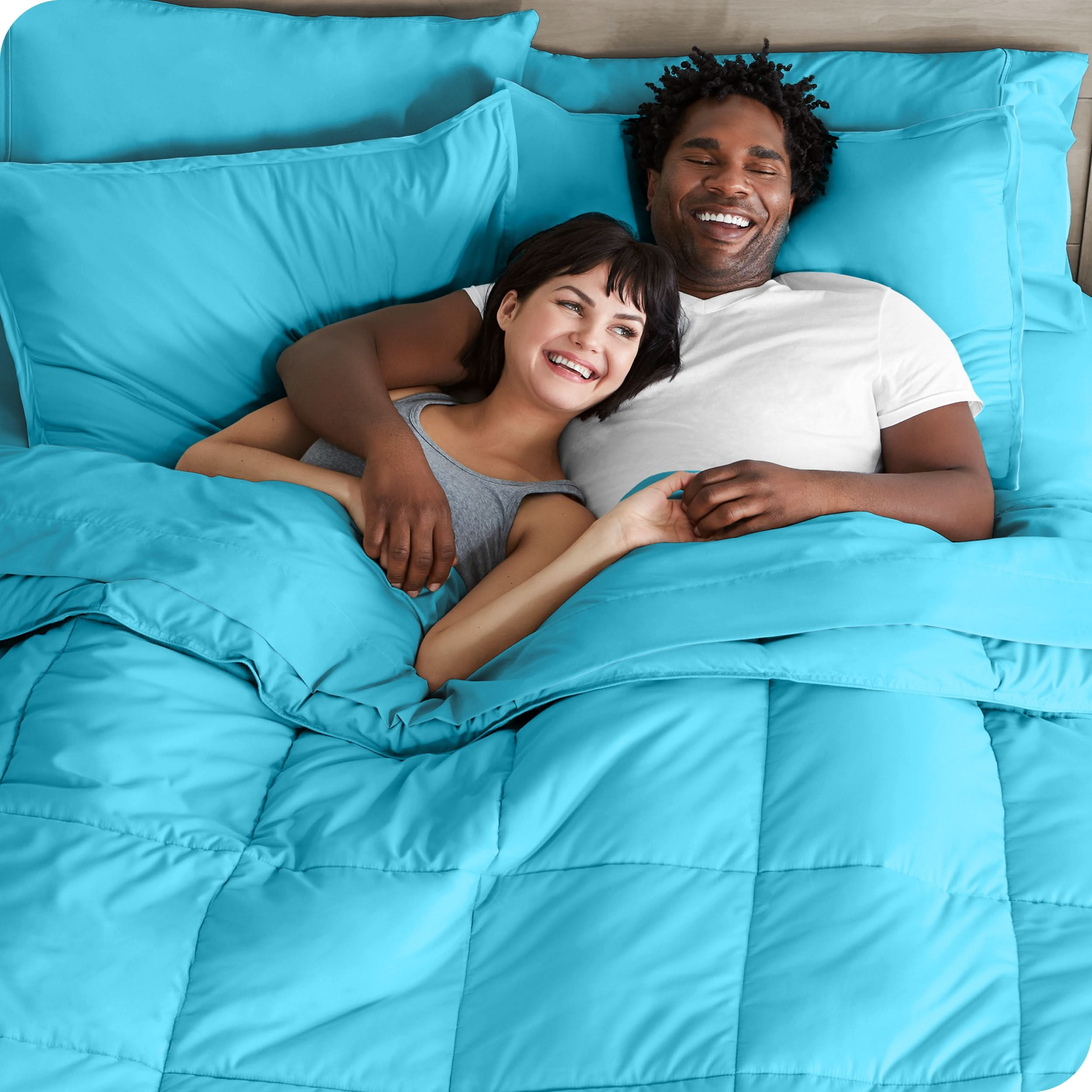 A couple is lying in bed with a comforter and sheets over them