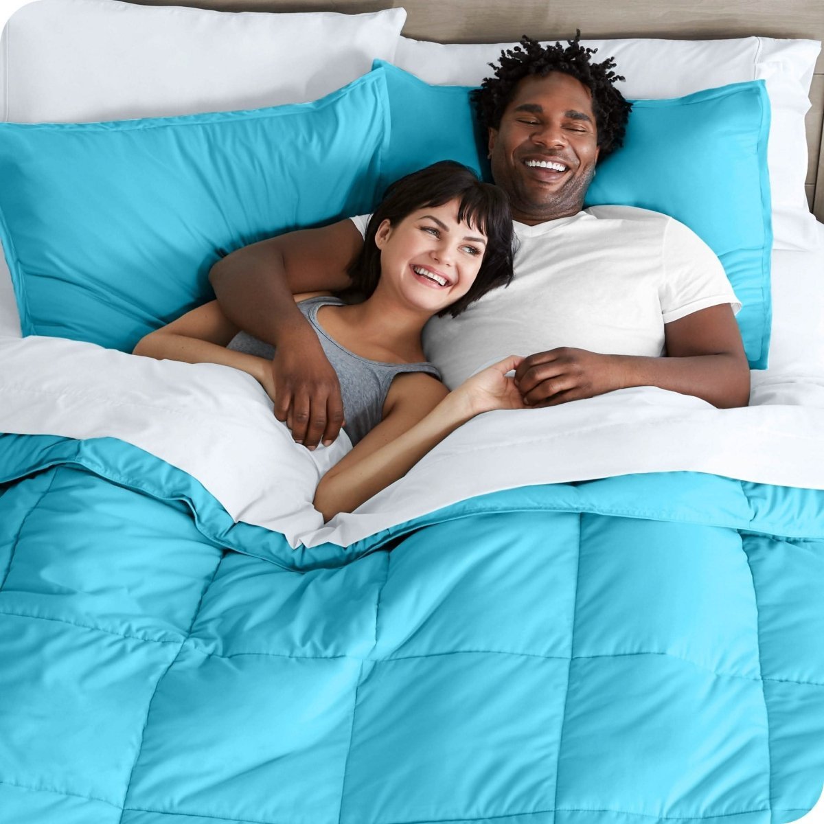 A couple is lying in bed with a comforter and sheets over them
