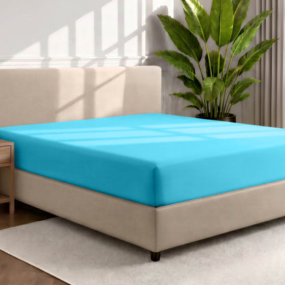 Bed with a fitted sheet in a room with a large plant and rug