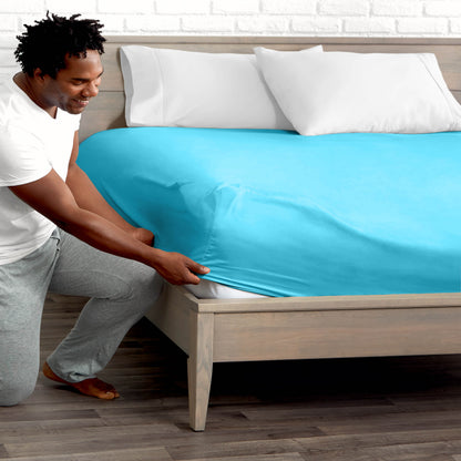 Man adjusting fitted sheet on a bed with white pillows.
