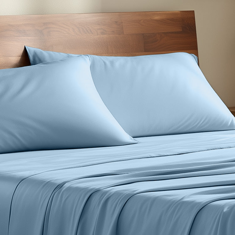 Blue bed sheets and pillows on a wooden bed frame against a beige wall.