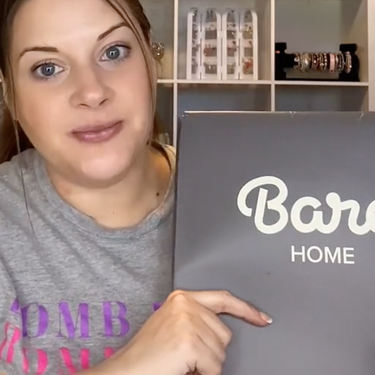Person holding a 'Bare Home' box in front of a shelf with decorative items.